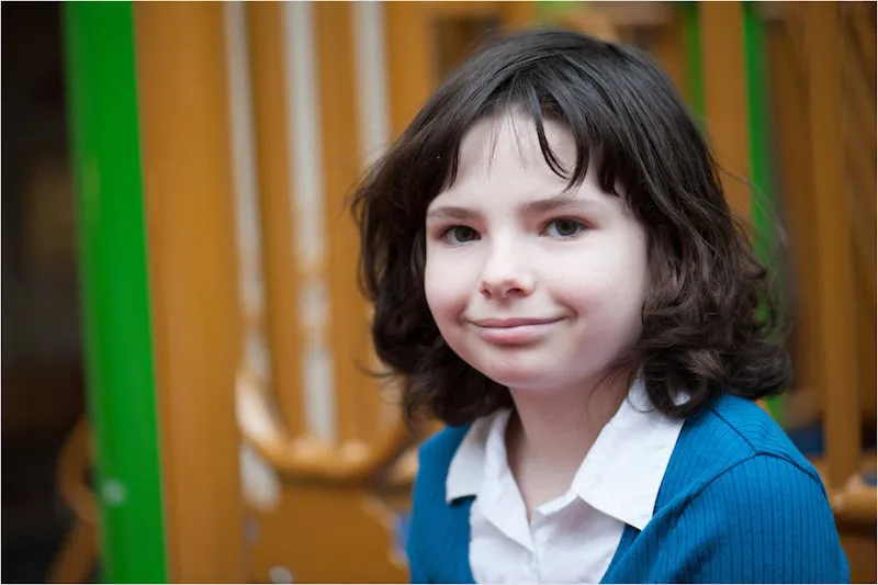 Girl with medium-length hair is sitting, wearing a cardigan sweater and an open collared button-down shirt