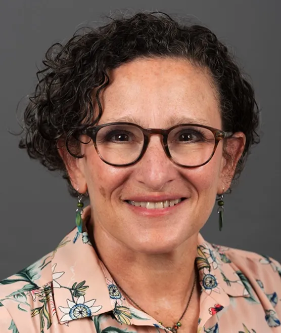 Headshot of Carol Weitzman, a woman with short curly hair and glasses. 